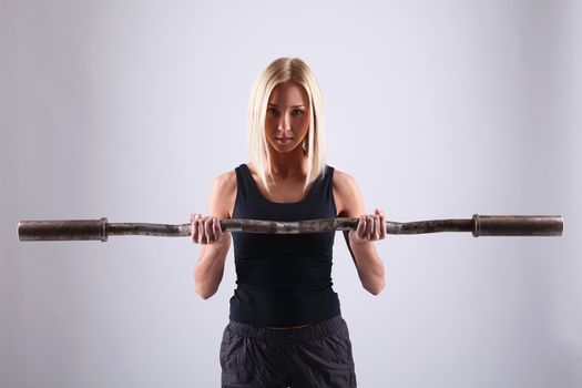 Slim and sporty young blonde doing fitness exercise with fitbar in studio