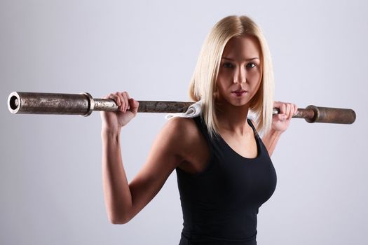 Slim and sporty young blonde doing fitness exercise with fitbar in studio