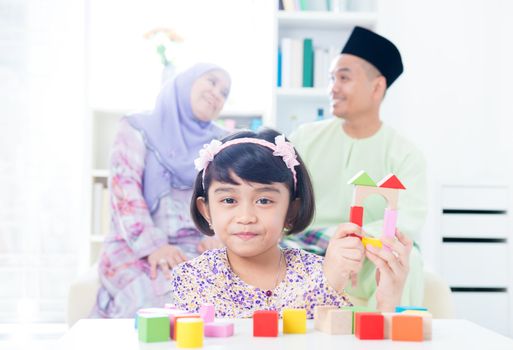 Muslim child building wooden house. Southeast Asian girl playing woodblock house at home.