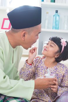 Cute Southeast Asian girl feeding yogurt to her father. Malay Muslim family lifestyle