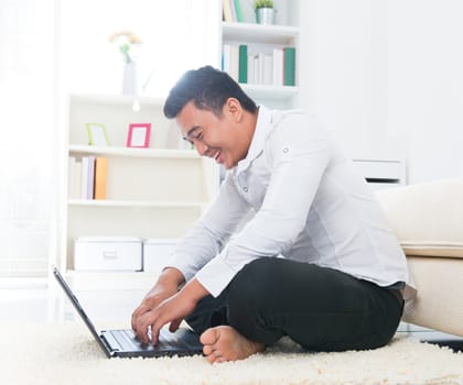 Southeast Asian man surfing internet at home, sitting on floor.