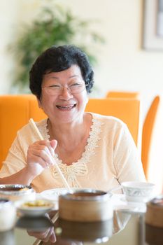 Happy 60s Senior Asian Woman dining indoors