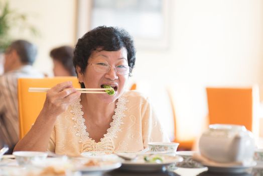 Happy 60s Senior Asian Woman eating vegetable at restaurant