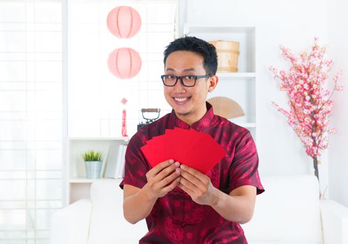 Southeast Asian Chinese man showing many red packets / ang pow indoors