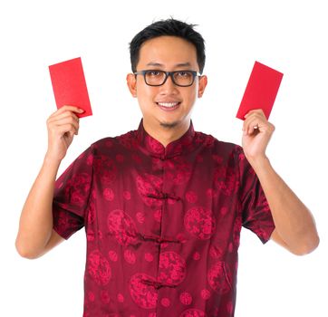 Happy Southeast Asian Chinese male in cheongsam hands holding two red packets / ang pow, isolated on white background.