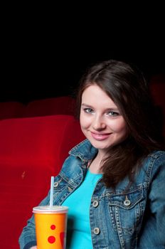 beautiful woman in a movie theater, watching a movie and drink a drink