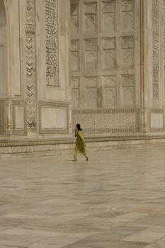 Indian woman in green sari walking past the Taj Mahal. White marble mausoleum in Agra, India.