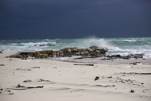 Dark clouds over a sunlit stormy sea and sandy beach on Cape Peninsula of South Africa.