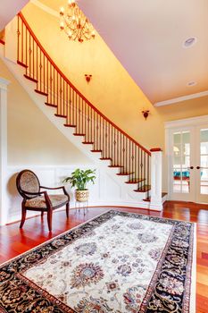 Home interior Entrance with curved staircase and luxury rug with chair.