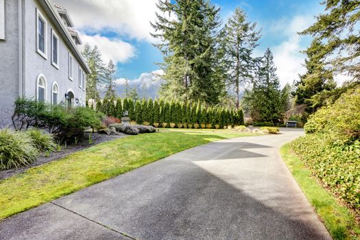 Home exterior of large grey classic house with many narrow windows and long driveway.