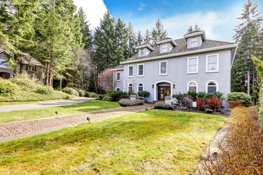 Home exterior of large grey classic house with pine trees.