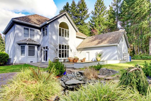 Home back exterior of large grey classic house with pine trees. 