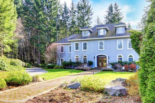 Home exterior of large grey classic house with pine trees.