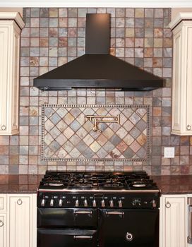 Large black kitchen stove with stone tiles and white cabinets.