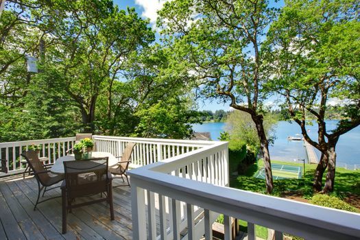 Large balcony home exterior with table and chairs, lake view.