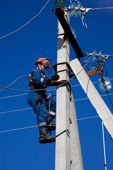 Electrician in overalls rises to concrete pole