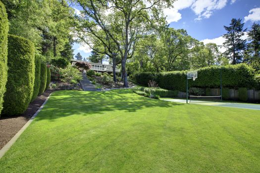 Tennis court with house on the hill  and bright green grass.