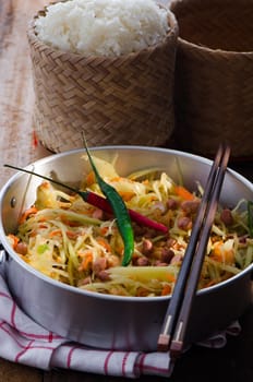 Thai very hot papay salad with a pot of sticky rice on woode table