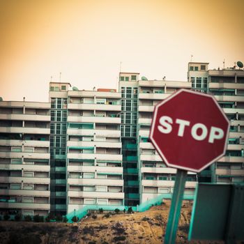 Moble photography lo-fi styled image of blurry stop sign in front of huge concrete high-density apartment complex