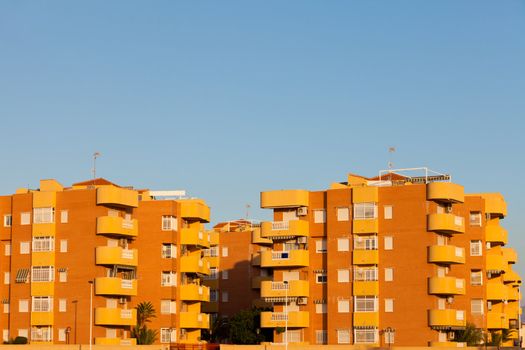 Group of multistorey colorful yellow-orange modern architecture apartment blocks in sunshine against a clear blue sky with copyspace