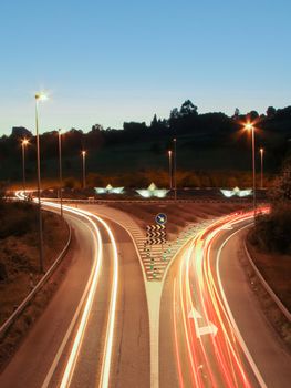 Car light trails on the road at night and illuminated paper boats in a roundabout in background