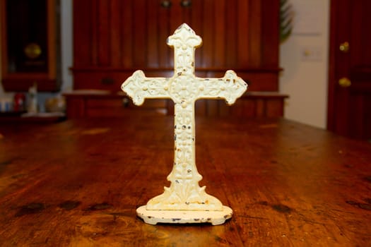 A very old antique white cross photographed on a wood dining table.