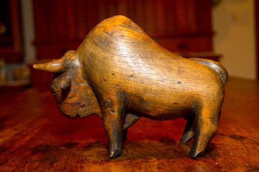 A hand carved wooden bull or buffalo statue on an antique wooden table.