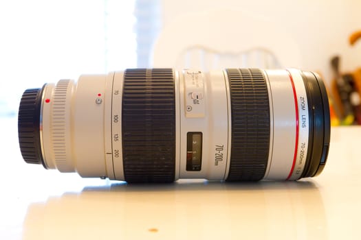 A white telephoto lens sits on a table while detached from the camera.