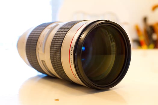 A white telephoto lens sits on a table while detached from the camera.