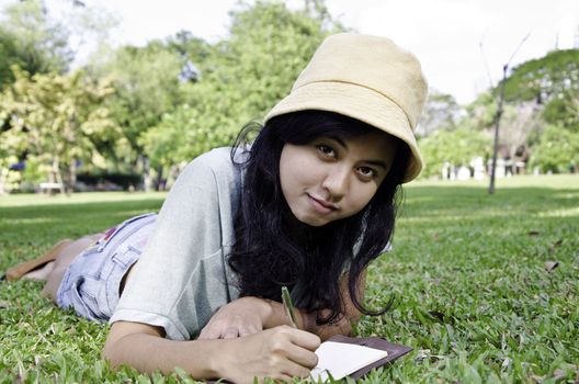 Young beautiful woman lies on green summer meadow with book 