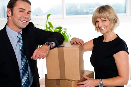 Office colleagues happily posing with their hands placed on packed cartons, relocation concept.