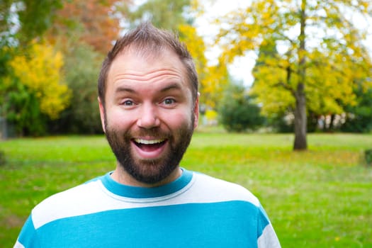 A portrait of a smiling man with a full beard outdoors in a park setting.