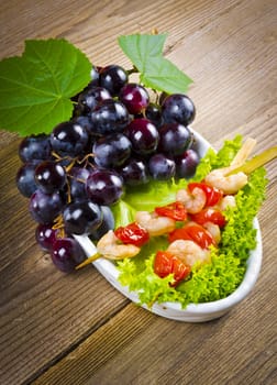 Grilled shrimp spits with bunches of grapes, tomatoes and green salad