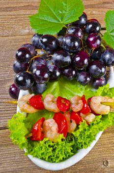 Grilled shrimp spits with bunches of grapes, tomatoes and green salad