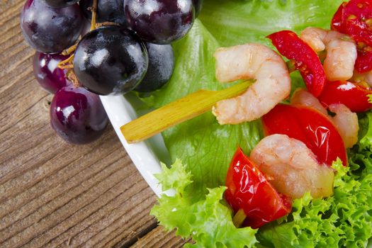 Grilled shrimp spits with bunches of grapes, tomatoes and green salad