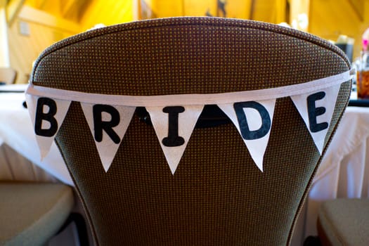 This chair at a wedding has a banner of flags that spell out the word bride to reserve her dinner seat.