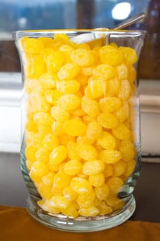 Yellow lemon drops are in a glass vase at a wedding at a candy bar.