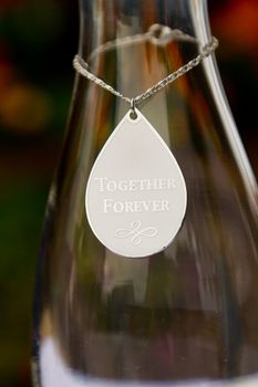 A small necklace hangs on a glass vase at a wedding and reads "together forever" before sand is put into the vase during the ceremony.