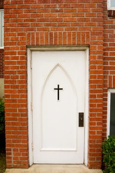 A church building has a white door with a cross on it for the entry to the religious facility.