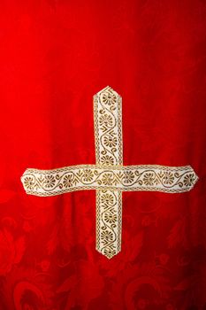 A gold and white cross is sewn onto a red robe that a priest wears.