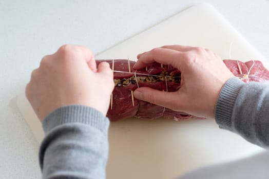 beef stuffed with mushroom filling being laced using a string between the toothpicks