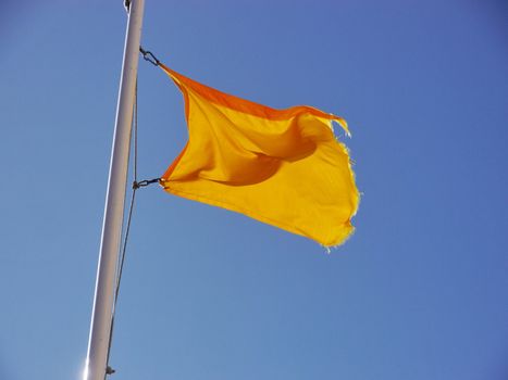 Yellow flag waving in the breeze against a blue sky.