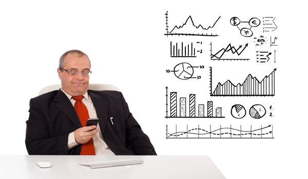 Businessman sitting at desk with diagrams and holding a mobilephone, isolated on white