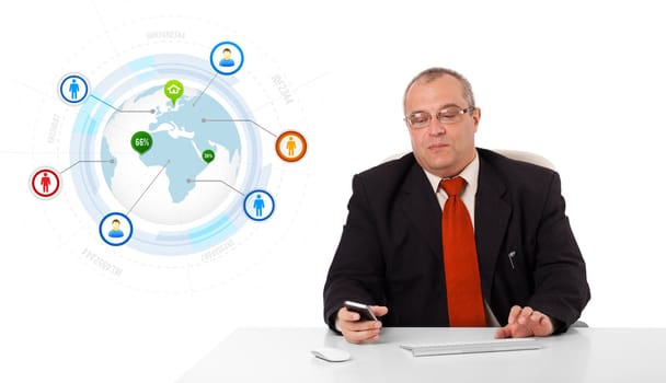 businessman sitting at desk and holding a mobilephone with globe and social icons, isolated on white