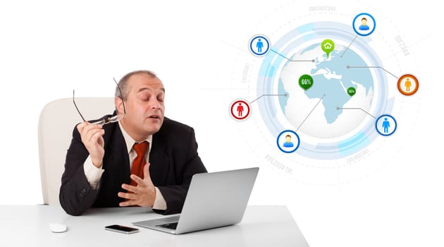 businessman sitting at desk and looking laptop with globe and social icons, isolated on white