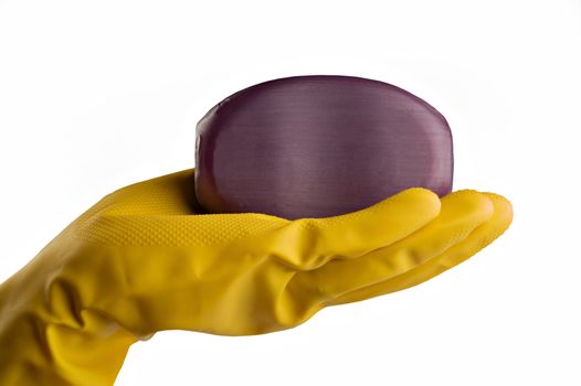 Hand in yellow protective utility glove holding purple or lavender bar of soap