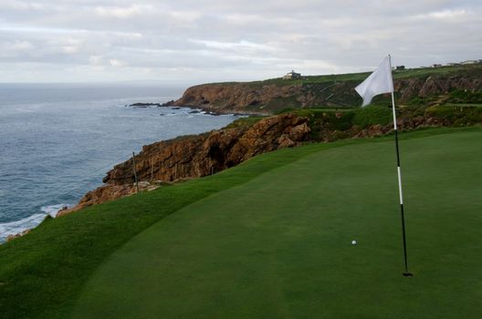 Seaside ocean holiday golf course with ball, pin, sea and hotel in background