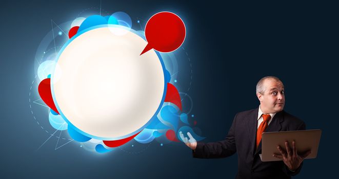 Businessman in suit holding a laptop and presenting abstract modern speech bubble with copy space