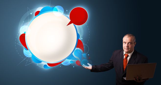 Businessman in suit holding a laptop and presenting abstract modern speech bubble with copy space
