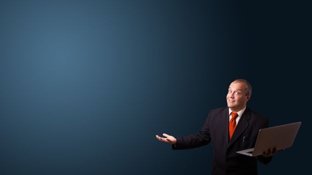 businessman in suit holding a laptop and presenting copy space